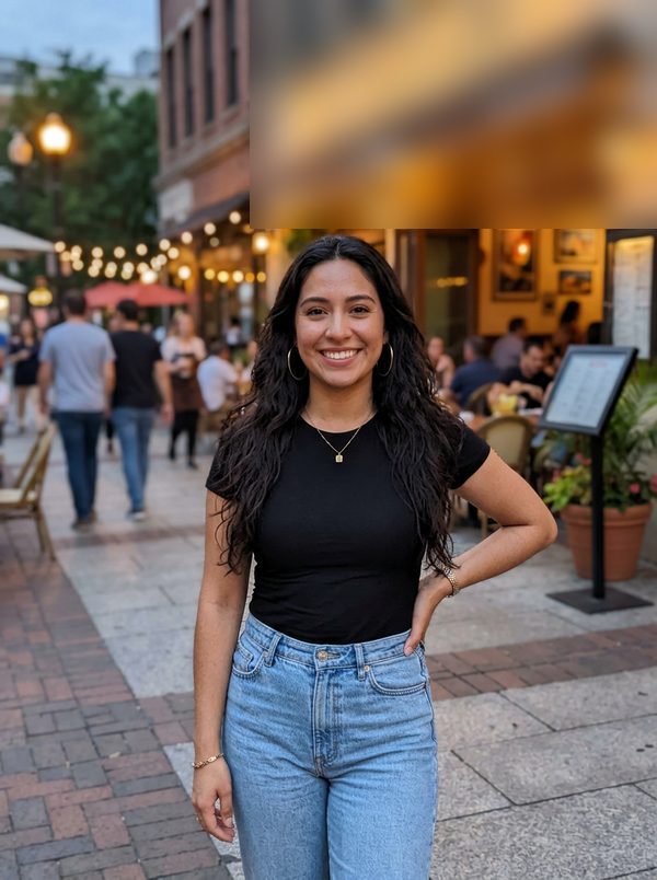 Evening street photo of a young woman with long curly hair, gold hoops and a black tee