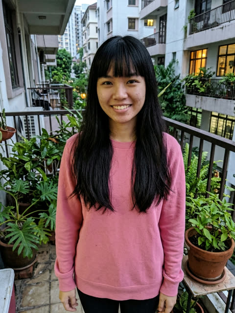 Photo of a smiling woman with long straight black hair and bangs in a pink sweatshirt